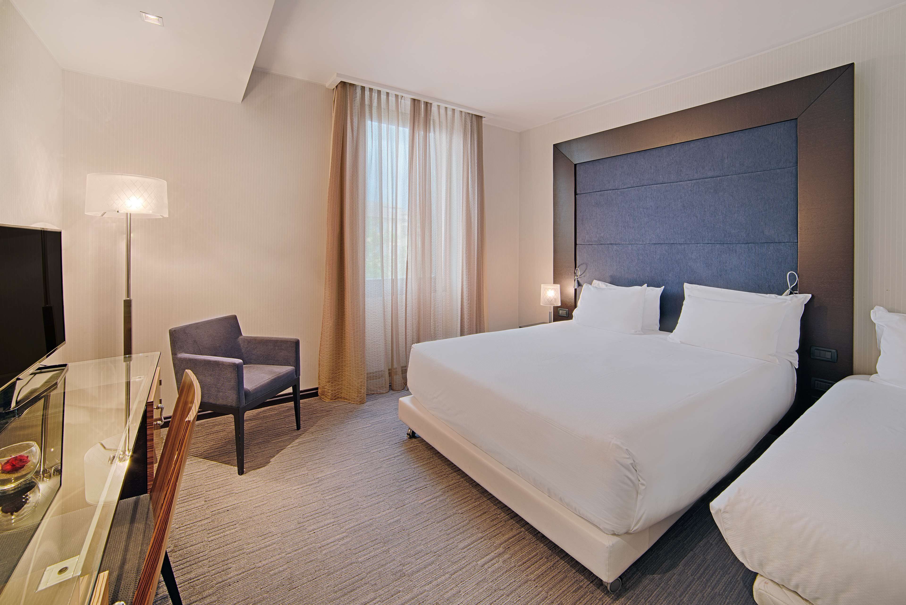 A hotel room with a large bed, a desk with a chair, a television, and a window with curtains.