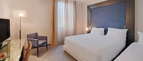 A hotel room with a large bed, a desk with a chair, a television, and a window with curtains.