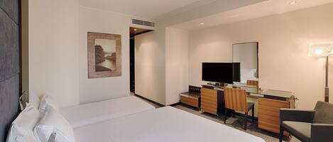 A hotel room with a large bed, a desk with a computer, a chair, a TV, and a painting on the wall.
