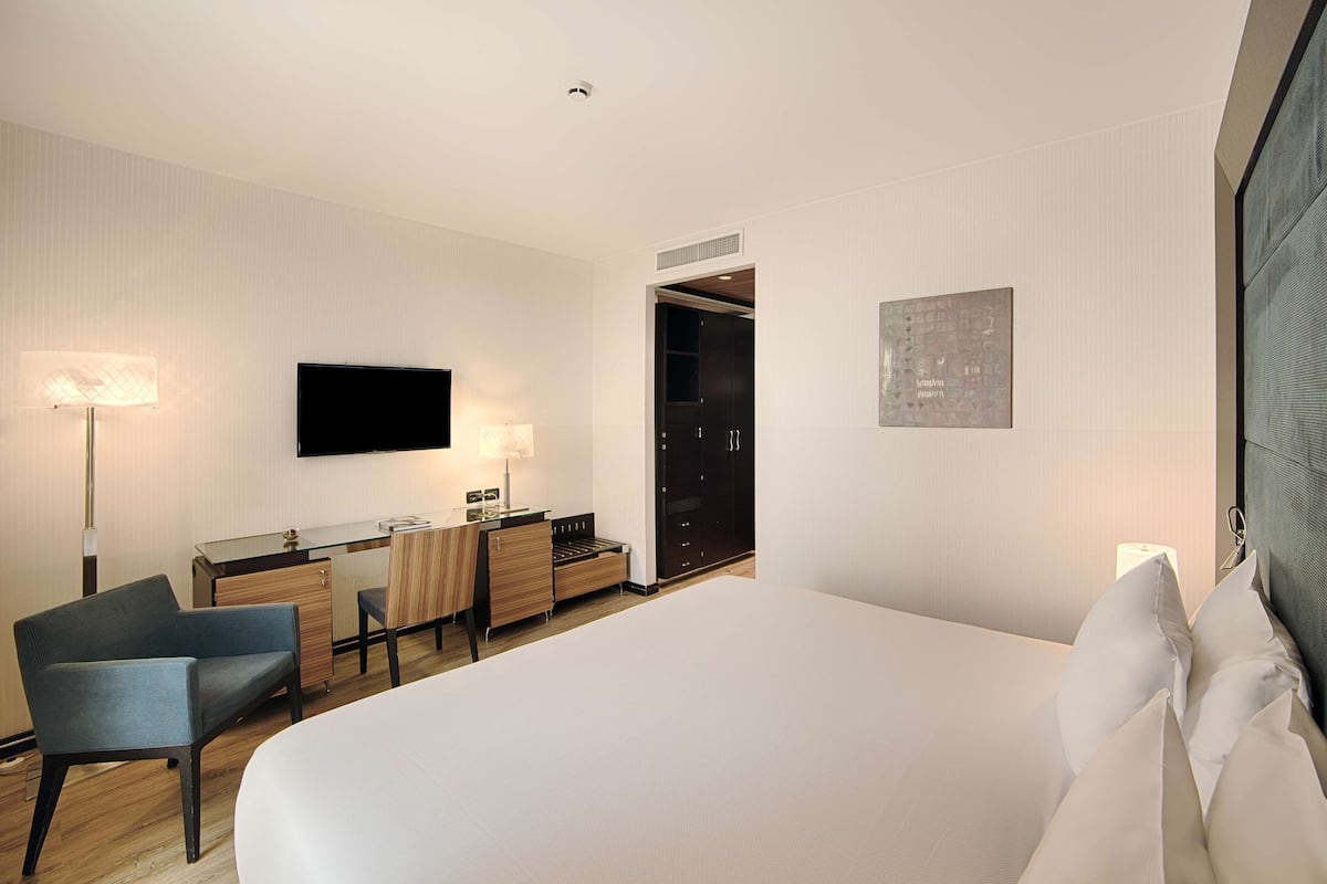 A modern hotel room with a large bed, a desk with a chair, a flat-screen TV mounted on the wall, and a walk-in closet.
