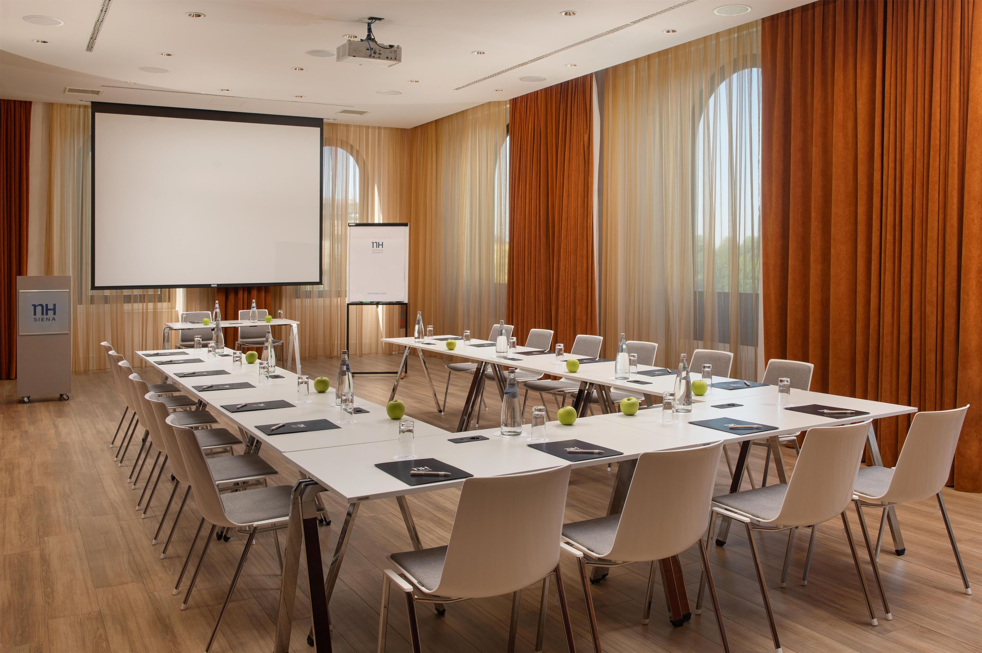 A conference room with a long table, chairs, a projector screen, and a presentation screen.