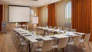 Un salón de conferencias con una larga mesa, sillas, una pantalla de proyector y una pantalla de presentación.