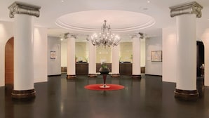 A spacious lobby with high ceilings, large columns, and a central chandelier.