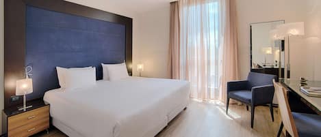 Ein modernes Hotelzimmer mit einem großen Bett, Nachttischlampen, einem Schreibtisch mit Stuhl und einem großen Spiegel.
