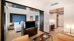 A modern hotel room with a large bed, a flat-screen TV, a coffee table, and a seating area with two chairs.