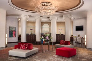 A lobby with a chandelier, columns, sofas, and a reception desk. - NH Siena (Siena)