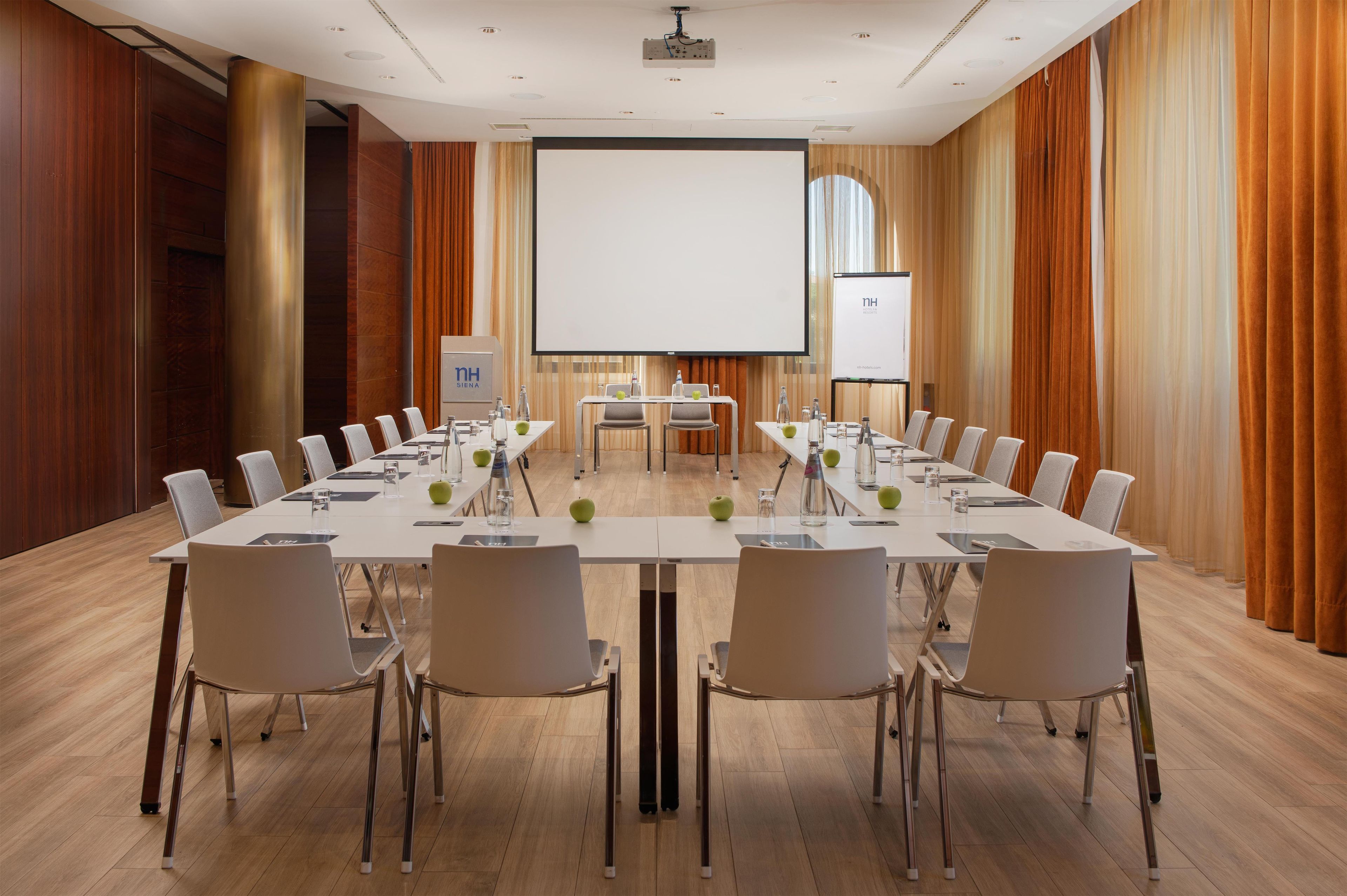 A conference room with a long table, chairs, a projector screen, and a presentation screen.
