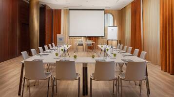 Un salón de conferencias con una larga mesa, sillas, una pantalla de proyector y una pantalla para presentaciones.