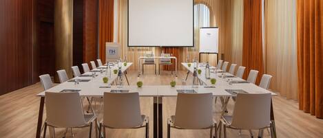 A conference room with a long table, chairs, a projector screen, and a presentation screen.