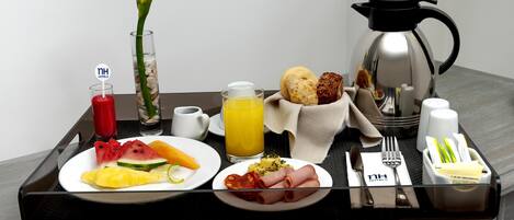 A breakfast tray with various food items, a coffee pot, a glass of orange juice, and a flower in a vase.