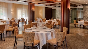 A spacious dining area with multiple round tables set for dining, surrounded by patterned chairs.