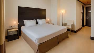Una habitación de hotel moderna con una cama grande, mesitas de noche, una silla y una puerta.