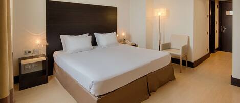 A modern hotel room with a large bed, bedside tables, a chair, and a door.