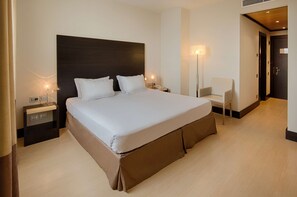 A modern hotel room with a large bed, bedside tables, a chair, and a door.