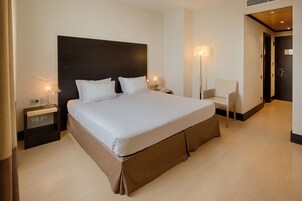 Una habitación de hotel moderna con una cama grande, mesitas de noche, una silla y una puerta.