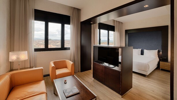A hotel room with a bed, a TV, a sofa, a coffee table, and a view of the city.