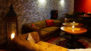 Un coin salon accueillant avec un mur orné de motifs, un canapé capitonné et une petite table décorée de bougies.