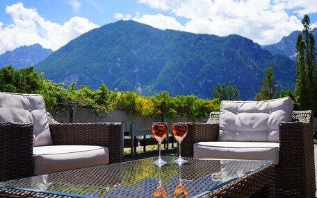 A glass table with two wine glasses, wicker furniture, and a mountain view.