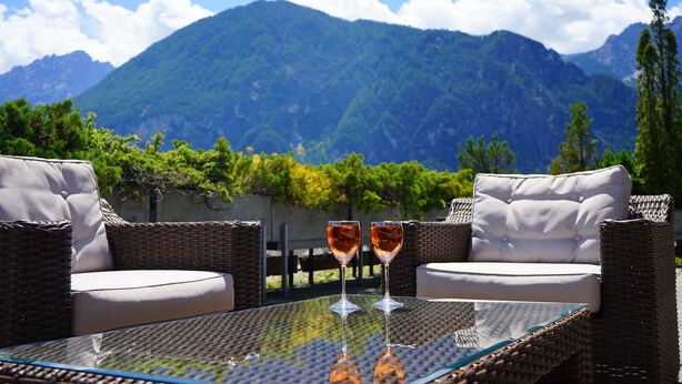 Une table en verre avec deux verres à vin, des meubles en osier et une vue sur la montagne.