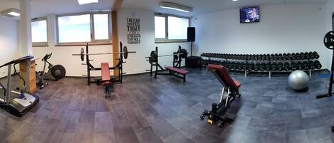 Ein Fitnessraum mit verschiedenen Trainingsgeräten, darunter Laufbänder, eine Hantelbank und Kurzhanteln.
