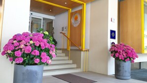 L’entrée d’un hôtel, avec un escalier, un comptoir d’accueil et de grands pots de plantes.