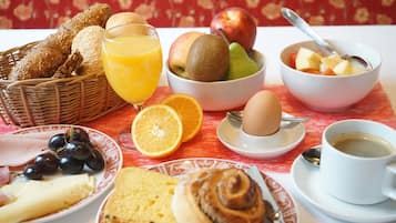 A breakfast table with bread, fruit, a glass of orange juice, a bowl of cereal, a plate of ham and cheese, and a cup of coffee.