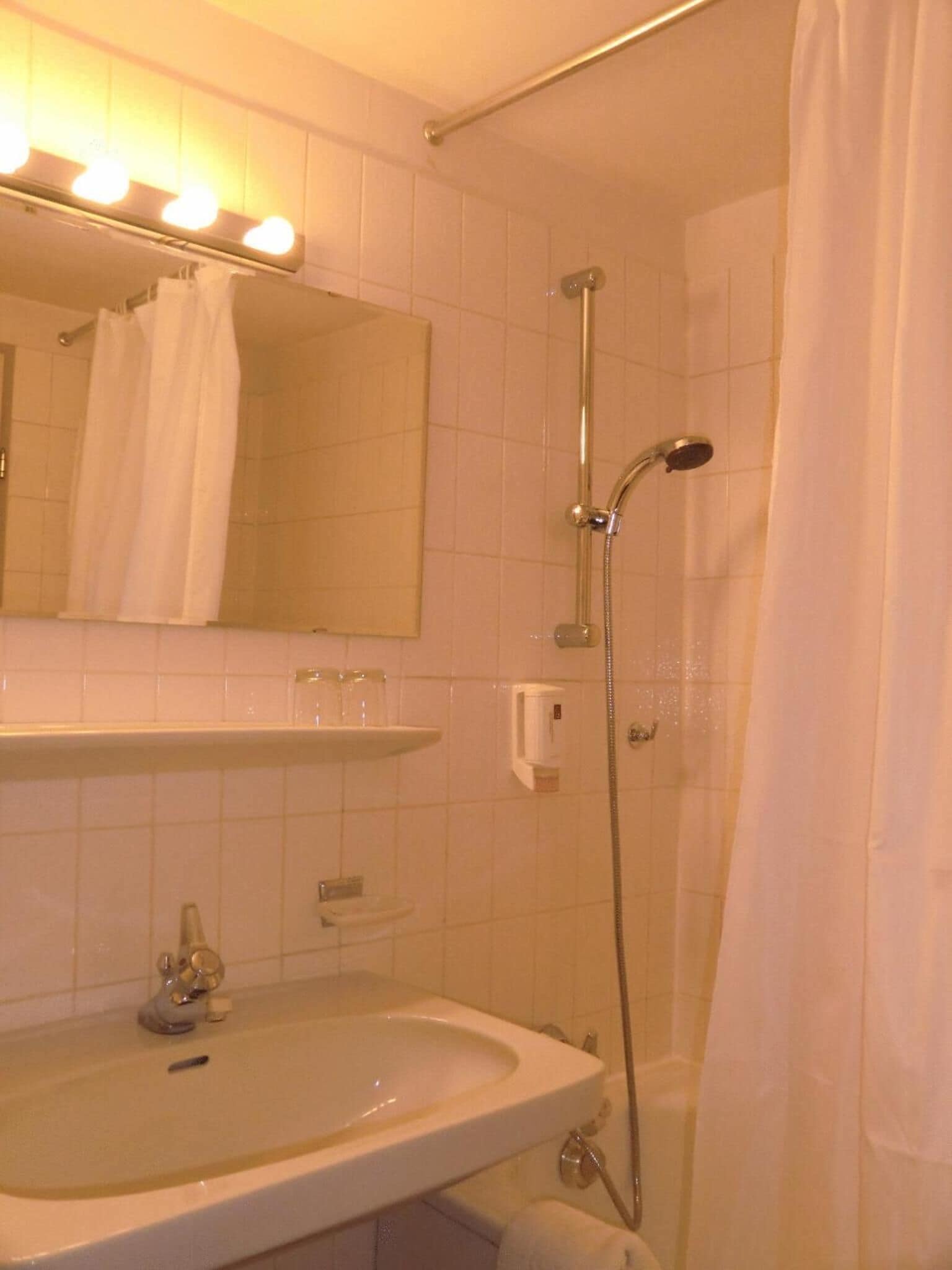 A bathroom with a sink, mirror, and shower.