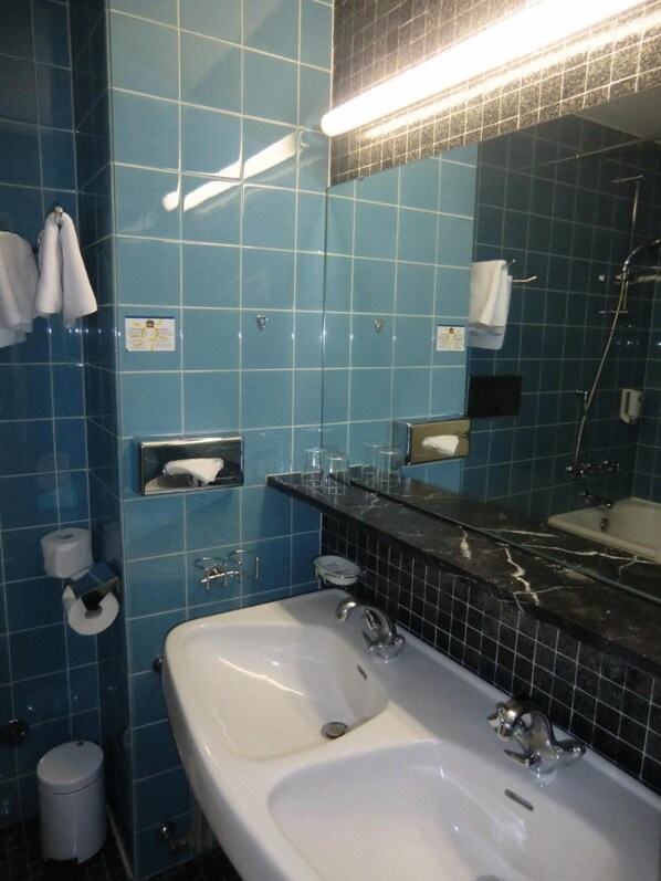 A bathroom with blue tiled walls, a white sink, a mirror, and a shower area.