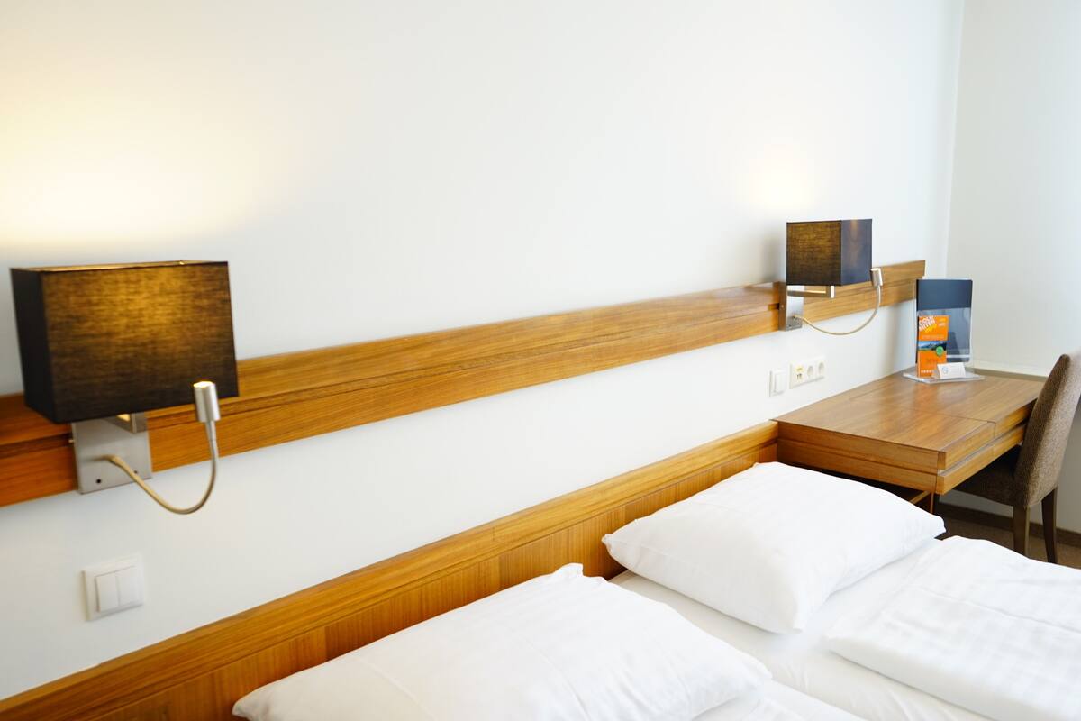 Ein Hotelzimmer mit einem hölzernen Kopfteil, einem Schreibtisch und einem Stuhl. Es gibt zwei Betten mit weißen Bettwäsche.