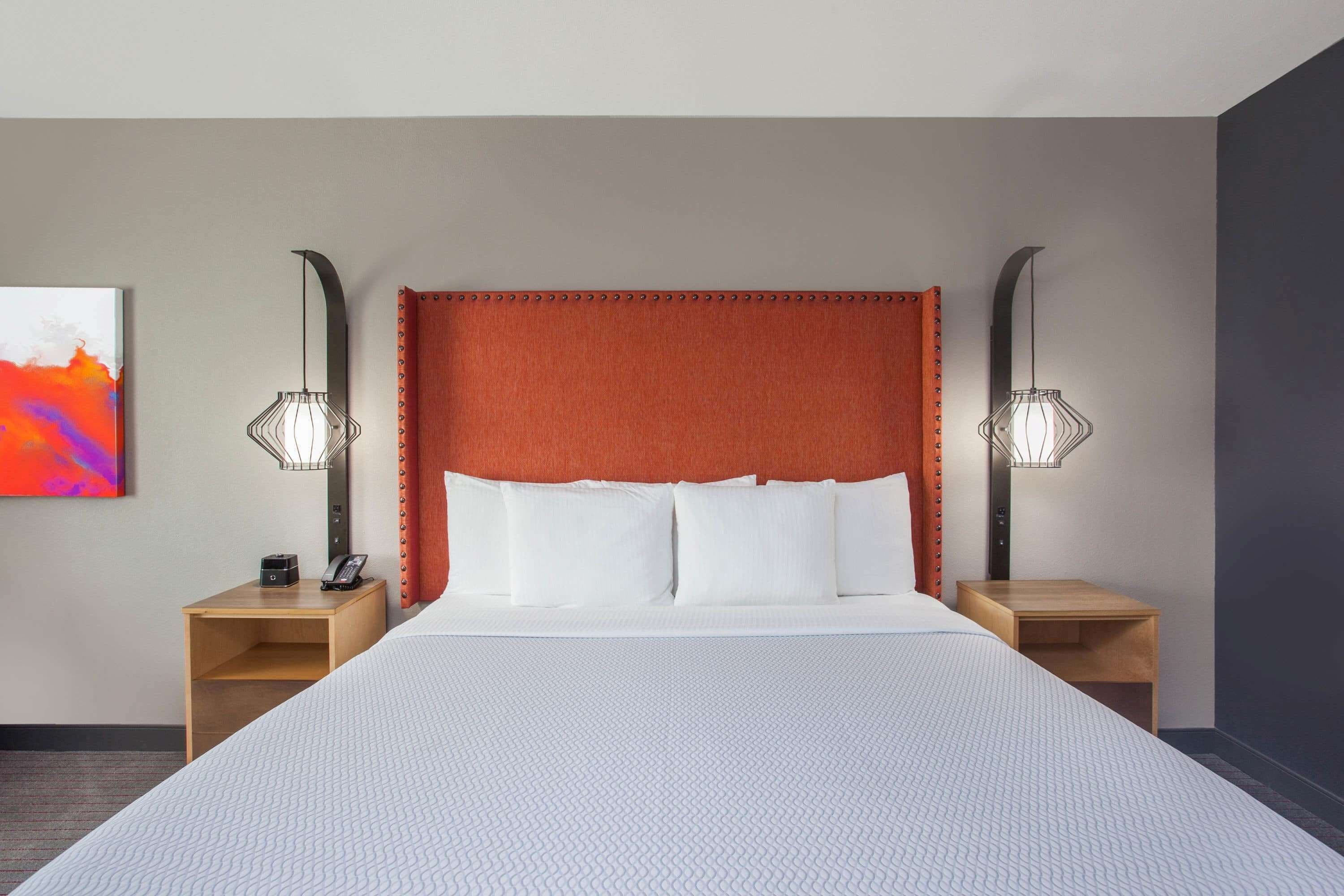 Een hotelkamer met een groot bed, twee nachtkastjes, een rode hoofdbord en twee wandlampen.