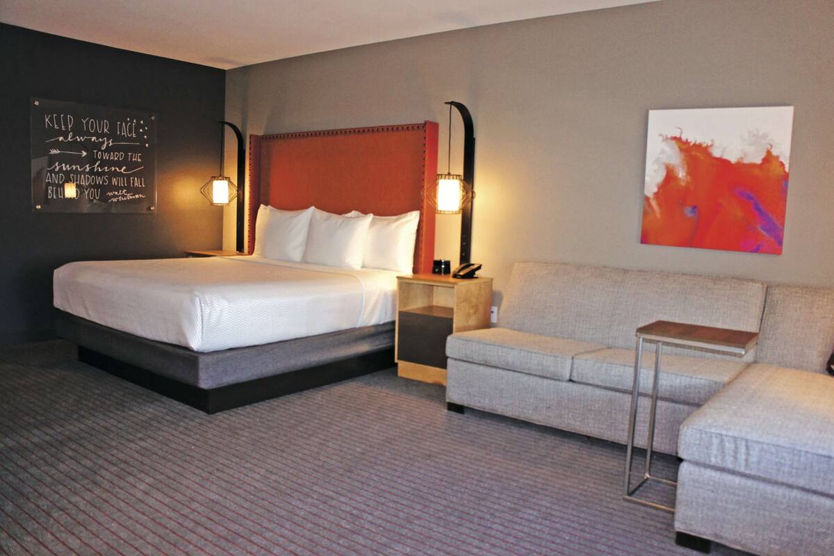 A hotel room with a large bed, a sofa, a nightstand, and a wall with a motivational quote.