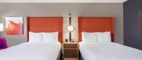 Habitación de hotel con dos camas, una mesita de noche con lámpara, un cuadro en la pared y una puerta a la derecha.