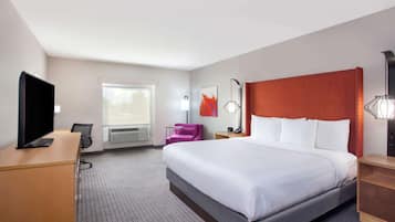 Quarto de hotel com uma cama grande, uma escrivaninha, uma televisão, uma cadeira e uma janela.