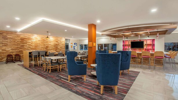 A modern dining area with wooden accents, blue chairs, and a large pillar. - La Quinta Inn & Suites by Wyndham Madera (Madera)