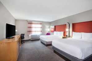 Habitación de hotel con dos camas, un escritorio con televisor, una silla, una ventana con cortinas y una lámpara.