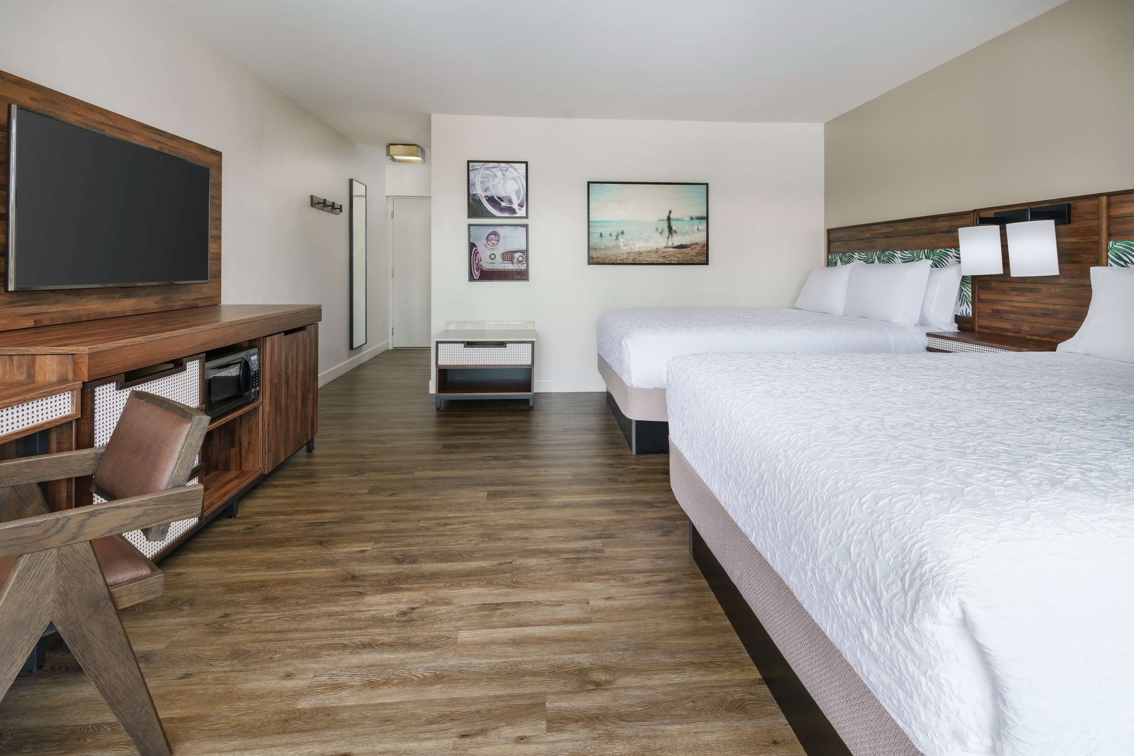 A hotel room with a wooden floor, a TV on a wooden stand, a bed with white bedding, and a small table with chairs.