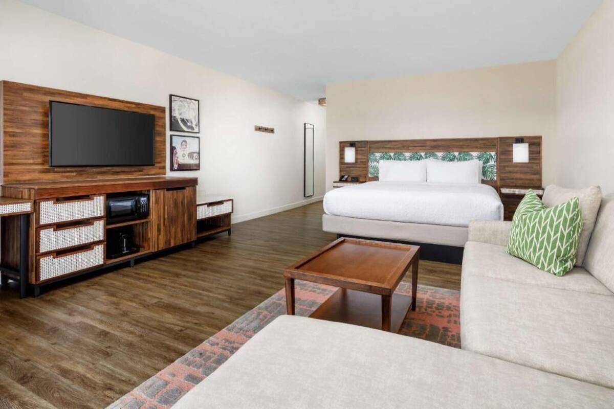 A hotel room with a bed, a sofa, a TV, a coffee table, and a wooden entertainment unit.