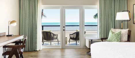 A hotel room with a balcony, a bed, a desk, and two chairs.