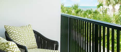 En balkon med fletmøbler og udsigt til havet og palmer.