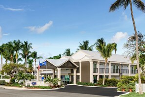 A hotel with a modern design, featuring a covered entrance, multiple floors, and a landscaped front with palm trees and shrubs.
