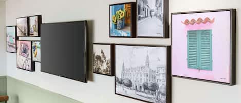 A wall with various framed artworks, including a large black screen, and a wooden table with chairs.