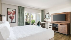 Habitación de hotel con una cama grande, un televisor montado en un mueble de madera y un balcón con vistas a palmeras.