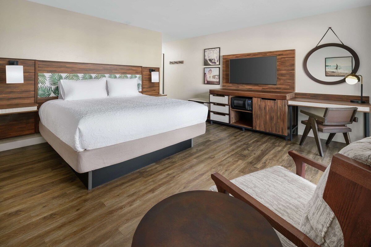 A bedroom with a bed, a desk, a chair, a TV, and a small table.