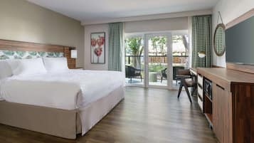 Habitación de hotel con una cama grande, un escritorio con silla, televisión y balcón con sillas.