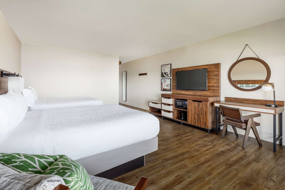 A modern hotel room with a large bed, a desk with a chair, a TV, and a mirror.