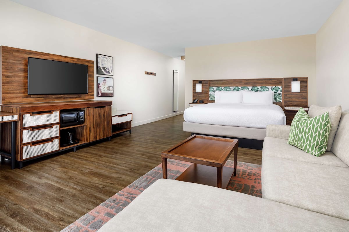 A modern hotel room with a large bed, a flat-screen TV, a wooden entertainment unit, and a small coffee table.