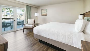 A hotel room with a large bed, a chair, a desk, and a view of a pool and palm trees through a sliding door.