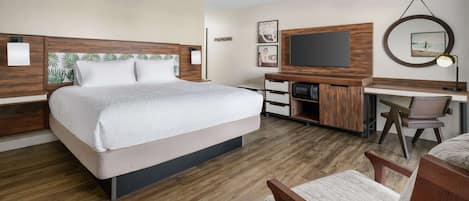A hotel room with a large bed, a desk with a TV, and a chair.