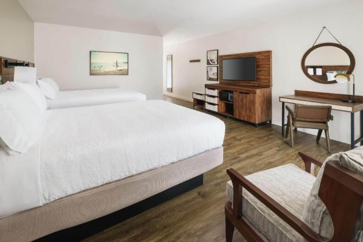 A hotel room with two beds, a desk, a chair, a TV, a mirror, and a picture on the wall.