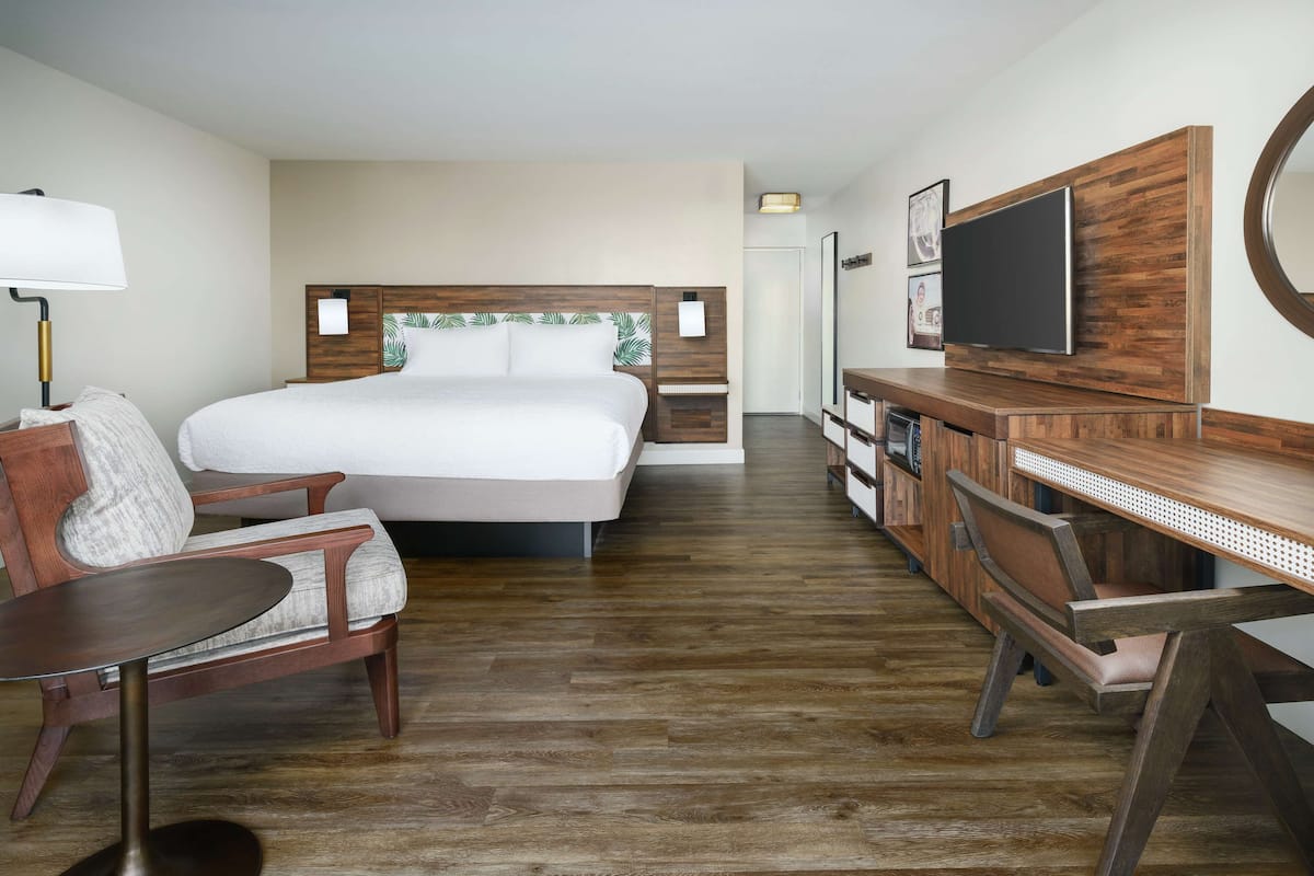 A hotel room with a large bed, a desk, a chair, a TV, and a lamp.